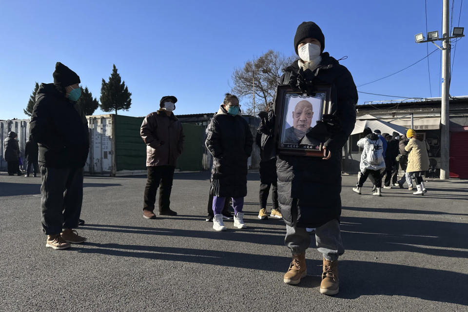 FILE - A family member carries the photo of a deceased relative outside a crematorium in Beijing, Saturday, Dec. 17, 2022. Nearly three years after it was first identified in China, the coronavirus is now spreading through the vast country. Experts predict difficult months ahead for its 1.4 billion people. (AP Photo/Ng Han Guan, File)