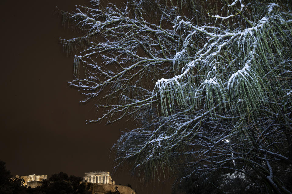 Snow covers a tree in central Athens with the ancient Parthenon temple on the Acropolis hill seen in the background , early Tuesday, Feb. 16, 2021. A cold weather front has hit Greece, sending temperatures plunging from the low 20s degrees Celsius (around 70 Fahrenheit) on Friday to well below freezing on Monday, and seeing snowfall in central Athens. (AP Photo/Petros Giannakouris)