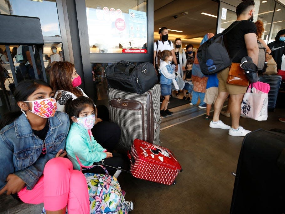 Young airline passengers sit on their luggage outside a terminal building.