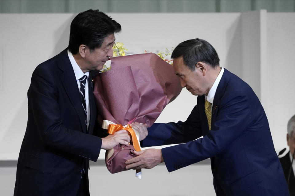 CORRECTS TO THAT JAPAN'S PRIME MINISTER SHINZO ABE RECEIVES FLOWER - Japan's Prime Minister Shinzo Abe, left, receives flowers from Chief Cabinet Secretary Yoshihide Suga after Suga was elected as new head of Japan's ruling party at the Liberal Democratic Party's (LDP) leadership election Monday, Sept. 14, 2020, in Tokyo. The ruling LDP chooses its new leader in an internal vote to pick a successor to Prime Minister Shinzo Abe, who announced his intention to resign last month due to illness. (AP Photo/Eugene Hoshiko, Pool)