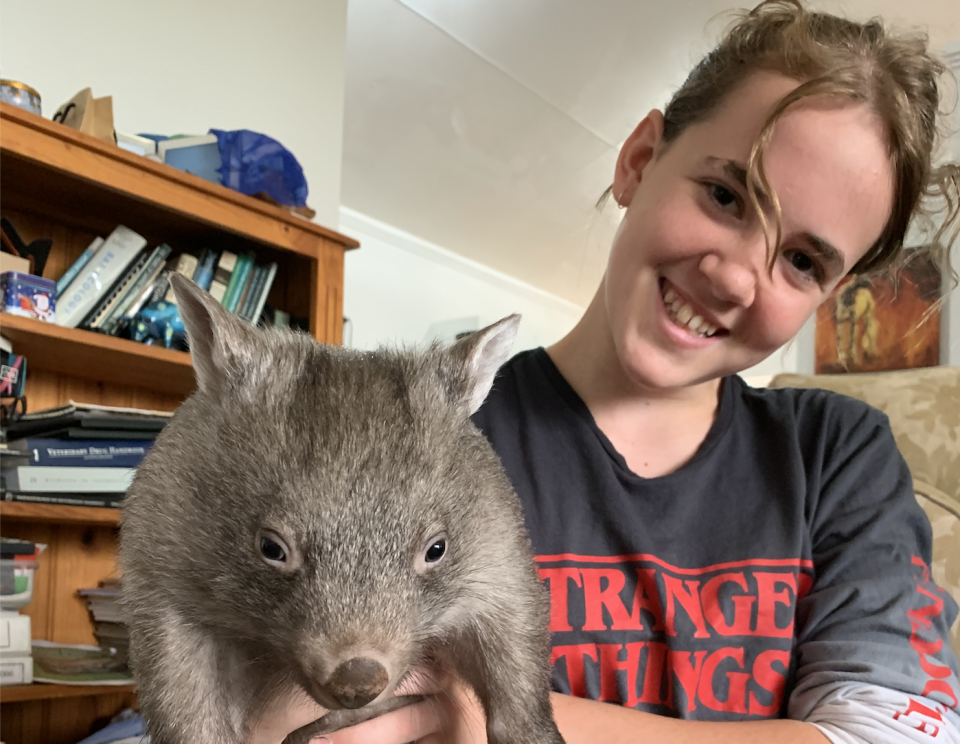 Eliza Hungerford wearing a Stranger Things top holds up a juvenile wombat. 