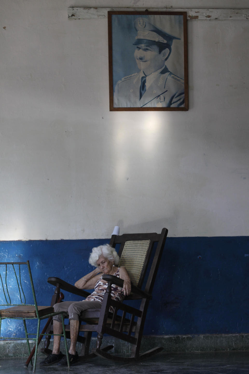 In this Feb. 5, 2014 photo, Carmen Zamora, who plays the part of Pachecho's widow, in the mock funeral known as the Burial of Pachencho, sits under a framed picture of Cuba's President Raul Castro as she waits for the start of the annual celebration in Santiago de Las Vegas, Havana, Cuba. The tradition was born on Feb. 5, 1984, when villagers got the idea of putting on a mock burial to mark the end of local carnival season. It took its name from the title of a play that had showed in what was then the town theater. "Pachencho" is not representative of any real person, living or dead, explained Alvaro Hernandez, head of a learning and recreation center that today is housed in the former theater. (AP Photo/Franklin Reyes)