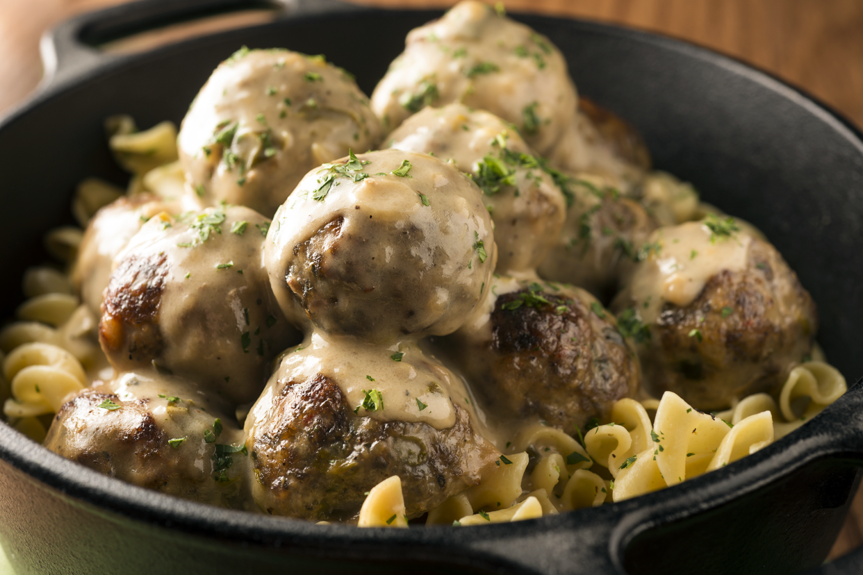 Closeup of Swedish meatballs in a cast iron skillet, selective focus, with a blurred background of a wooden table along the top