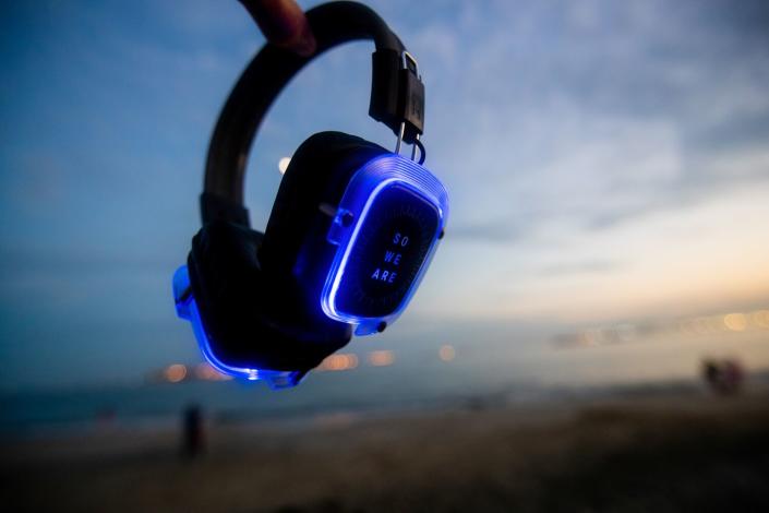 A detail image of glowing blue headphones used for silent disco dances, inscribed with the words &quot;So We Are.&quot;