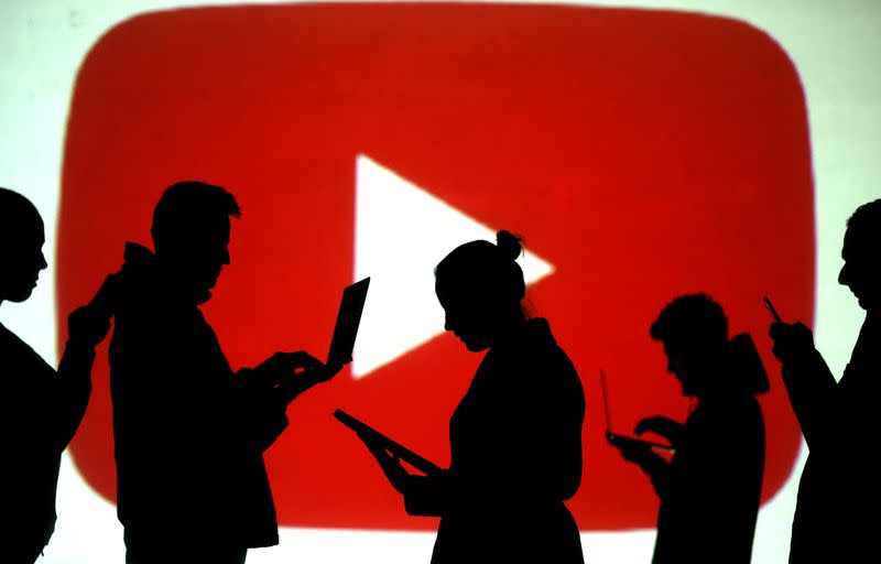 FILE PHOTO: Silhouettes of laptop and mobile device users next to a screen projection of the YouTube logo in this picture illustration