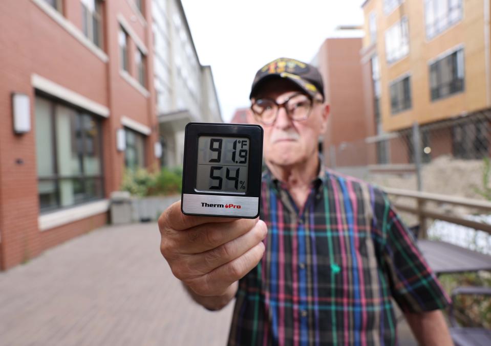 Dana Peltier, 75, who lives at Enso Flats in downtown Brockton, holds a temperature gauge that reads 91.9 degrees Fahrenheit during the afternoon on Thursday, July 28, 2022.