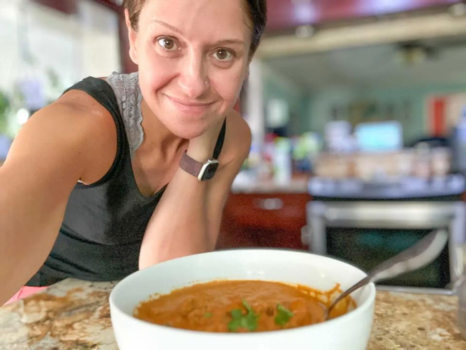 Selfie of the writer wearing a black tank top leaning over a kitchen counter with a white bowl of orange chicken curry in front of her