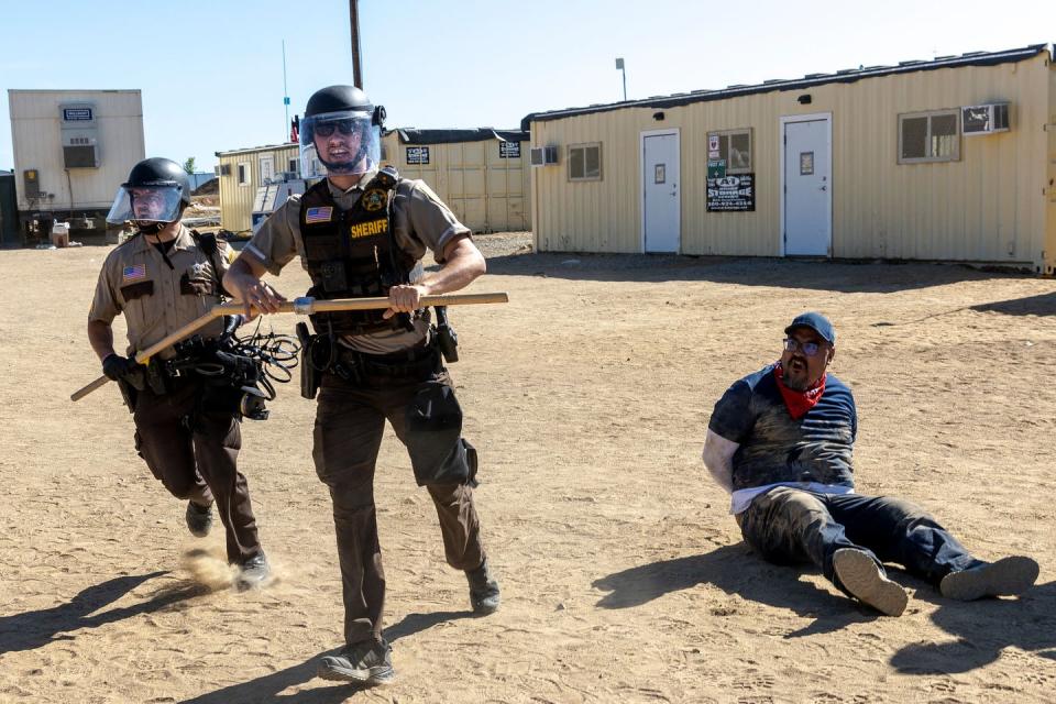 Two police in riot gear run while handcuffed man sits on ground