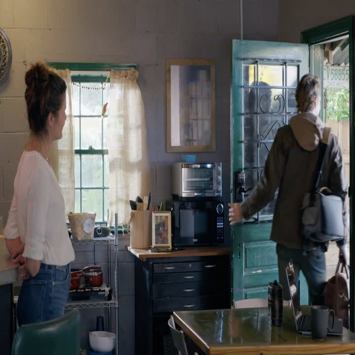 A woman watches a man leave through the front door of a house.