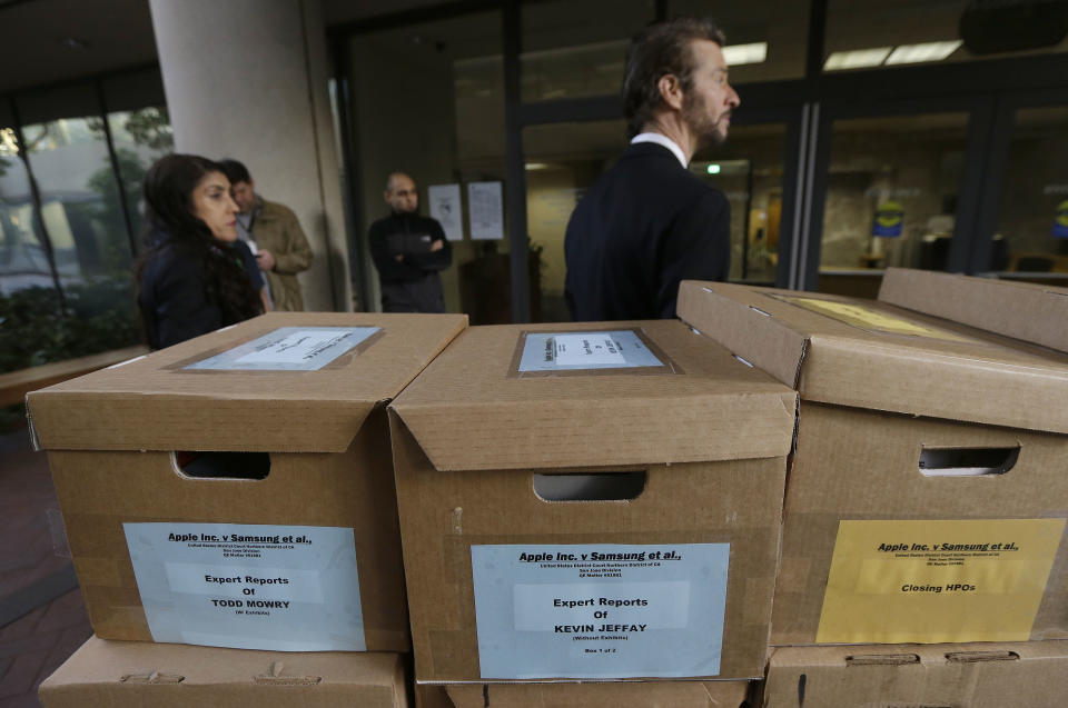 Clerks stand behind boxes containing documents related to the Apple Inc. versus Samsung case outside of a federal courthouse in San Jose, Calif., Monday, April 28, 2014. A federal court has delayed by a day closing arguments in the Apple and Samsung trial because of an appeals court ruling in another case on a related patent issue. Dueling expert witnesses were called back to the stand Monday in a San Jose federal courtroom to discuss whether the ruling in a legal dispute between Apple and Motorola has any effect on the Apple and Samsung trial. Lawyers will now deliver closing arguments Tuesday. (AP Photo/Jeff Chiu)