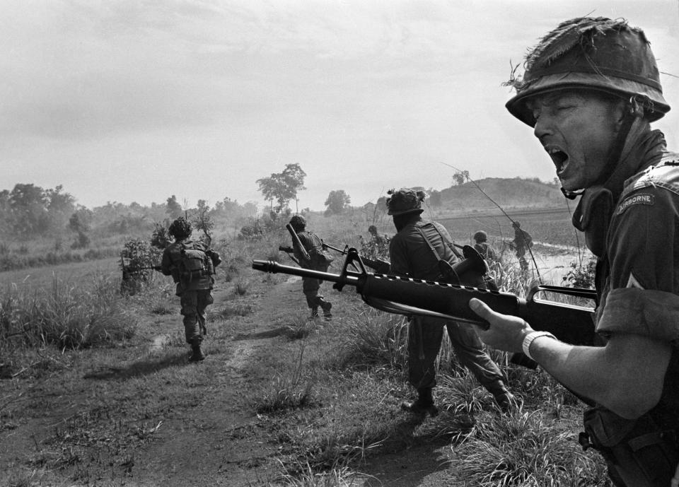 An American paratrooper sergeant shouts orders to his squad of the 2nd Battalion of the 173rd Airborne Brigade. The brigade charged across an abandoned road under heavy sniper fire, near Ben Binh, June 1, 1965. (AP Photo/Horst Faas)