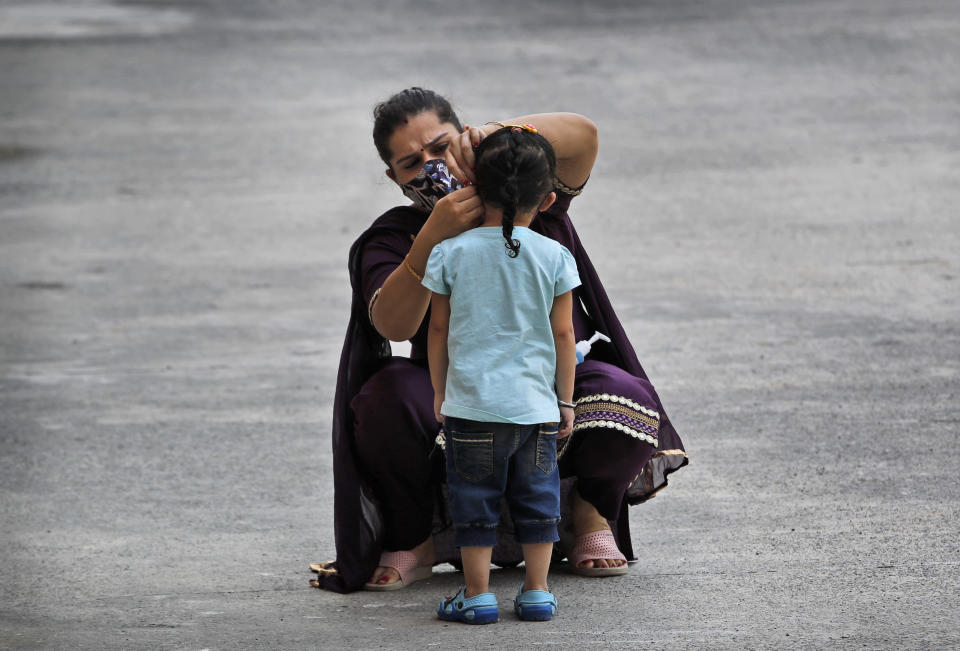 A woman fixes her daughter's face mask at a COVID-19 testing center in New Delhi, India, Saturday, Oct. 3, 2020. India has crossed 100,000 confirmed COVID-19 deaths on Saturday, putting the country's toll at nearly 10% of the global fatalities and behind only the United States and Brazil. (AP Photo/Manish Swarup)