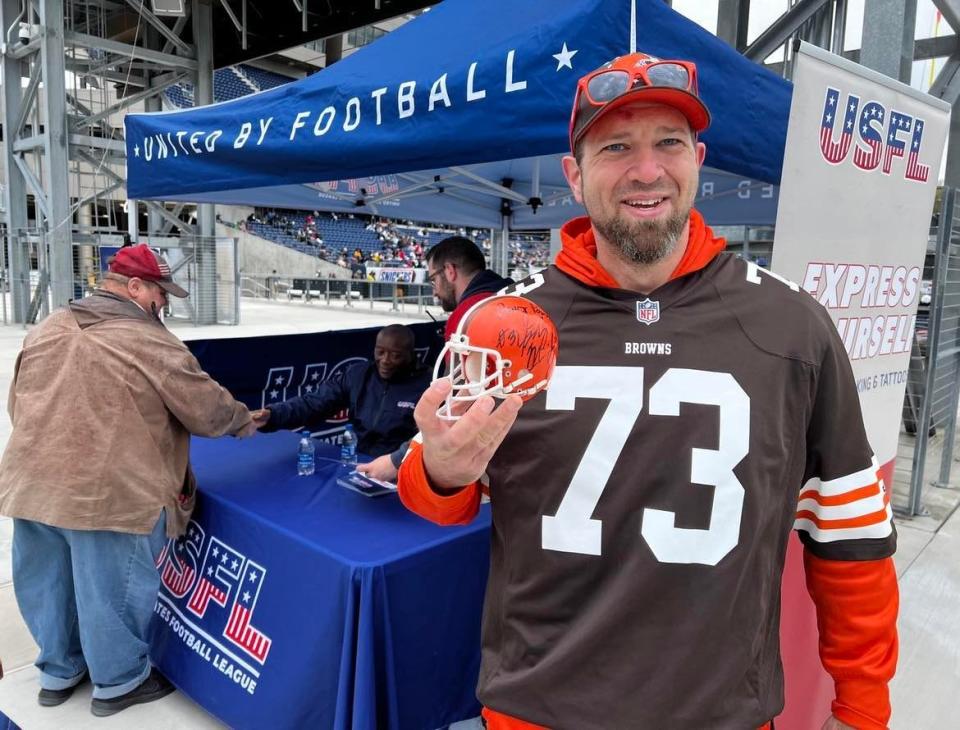 A Cleveland Browns fan poses for a photo after getting his small helmet autographed by Frank Minnifield, who played for the Browns in the 1980s and early '90s. Minnifield also played in the original USFL.