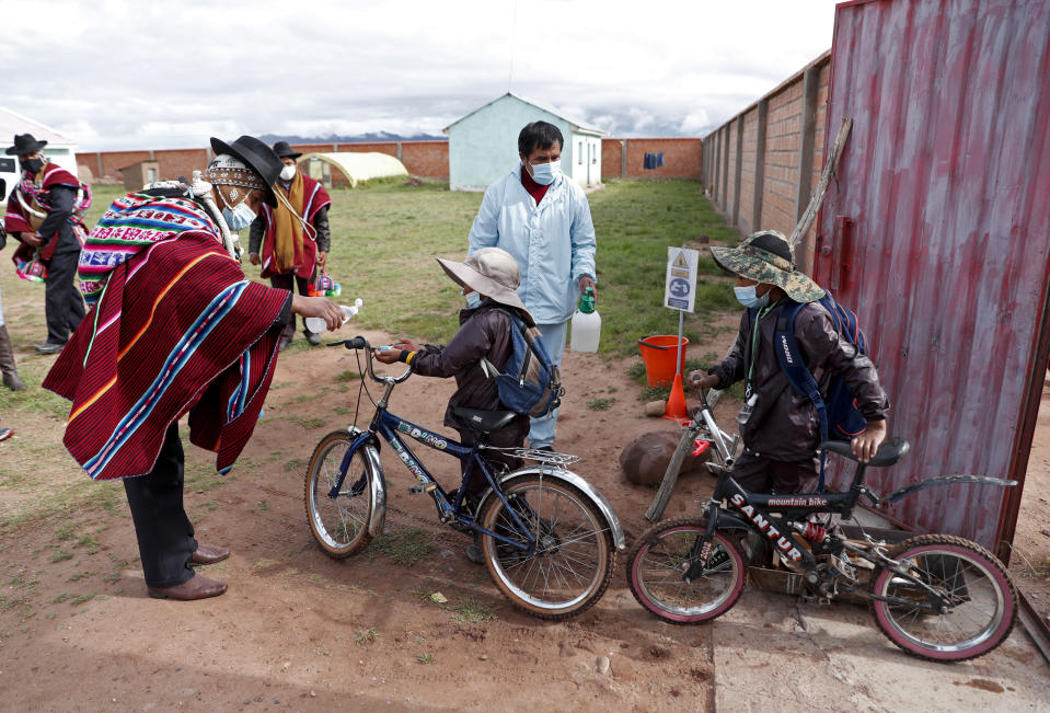 An Aymaran Indigenous parent gives anti-bacterial gel to students entering the Jancohaqui Tana school, where students are wearing new, protective uniforms as they return for their first week of in-person classes amid the COVID-19 pandemic, near Jesus de Machaca, Bolivia, Thursday, Feb. 4, 2021. (AP Photo/Juan Karita)