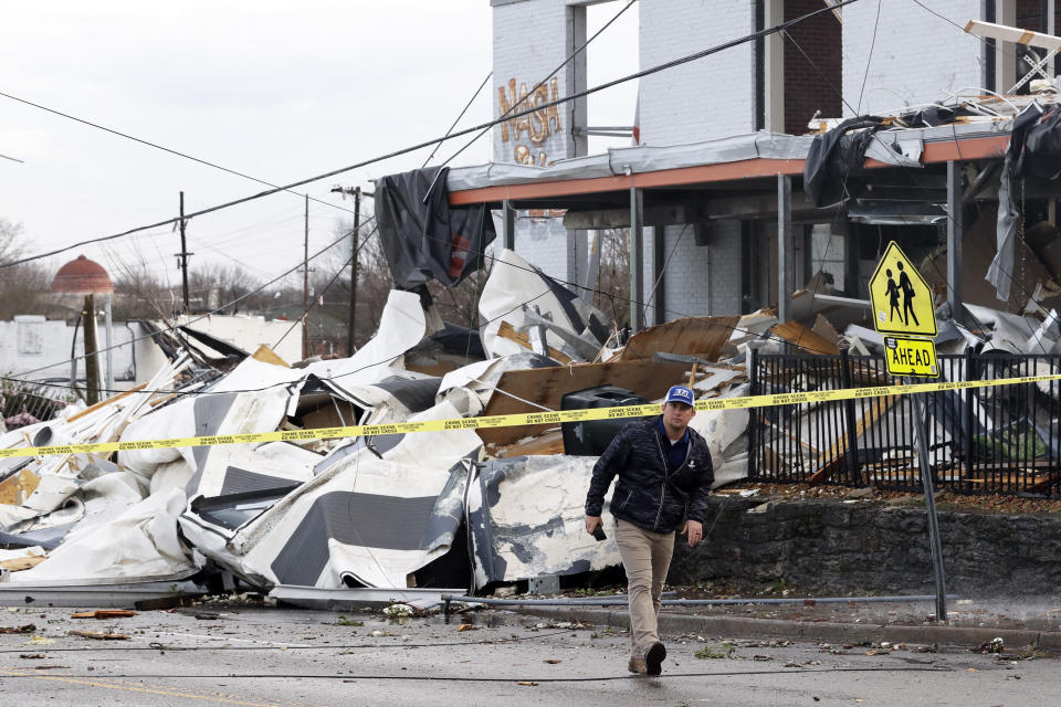 FILE - In this March 3, 2020, file photo, a man walks past storm debris Tuesday, March 3, 2020, in Nashville, Tenn. It has been nearly a year since deadly tornados tore across Nashville and other parts of Tennessee as families slept. The March 3 storm killed more than 20 people, some in their beds, as it struck after midnight. More than 140 buildings were destroyed across a swath of Middle Tennessee, burying people in rubble and basements. (AP Photo/Mark Humphrey, File)
