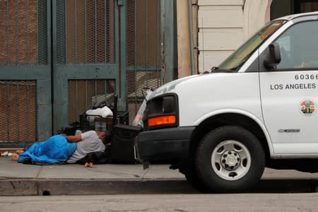 A homeless person sleeps on the sidewalk next to a Los Angeles County city vehicle in the skid row area of downtown Los Angeles, California