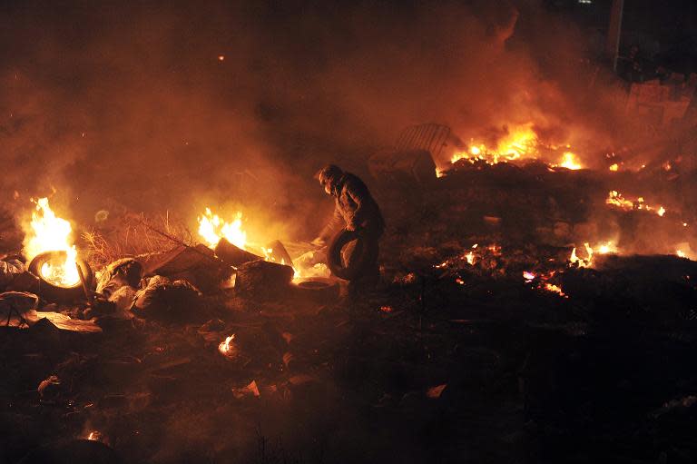 A protester throws tyres to keep a barriade of flames between protesters and police at Independence square in Kiev on February 19, 2014