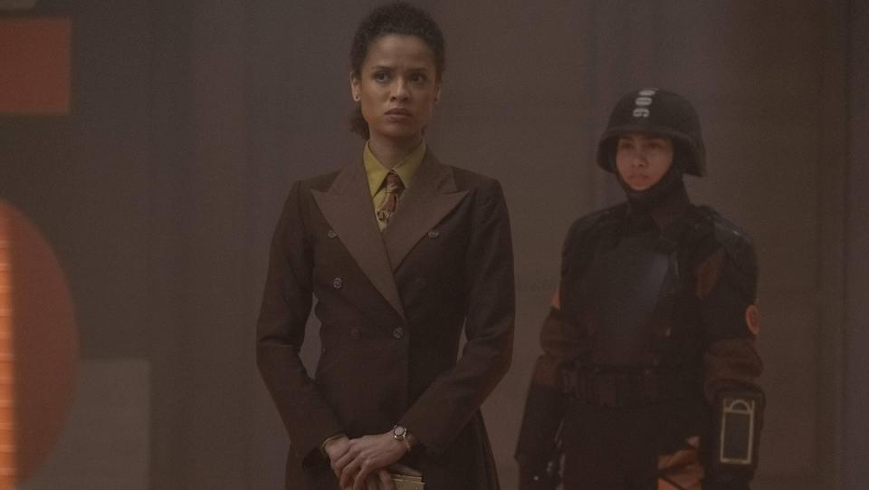 Renslayer (Gugu Mbatha-Raw) wearing a brown double-breasted suit and holding her Tempad, with another TVA agent behind her.