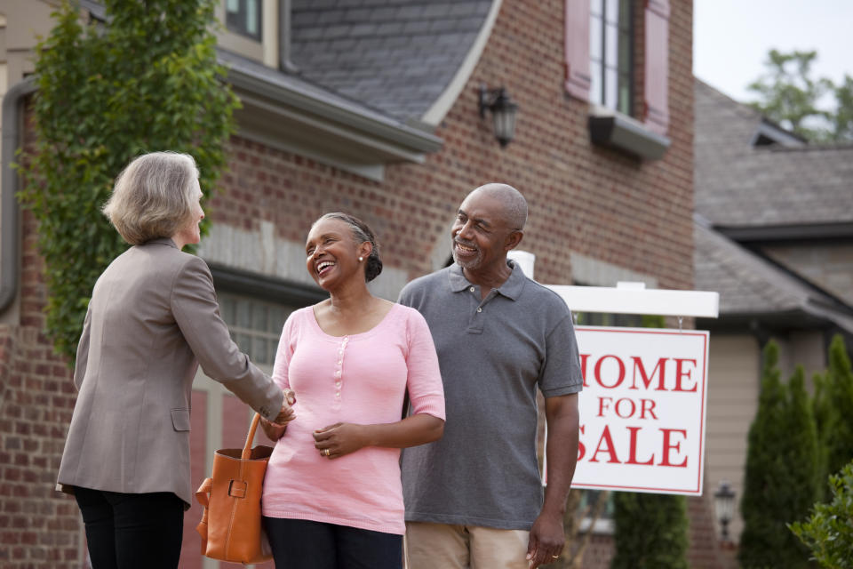 Realtor shaking hands with smiling couple outside house for sale