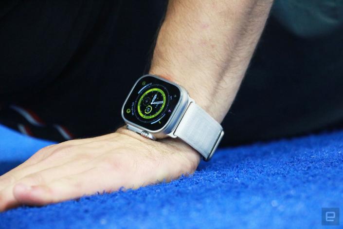 The Apple Watch Ultra with alpine loop on the wrist of a person doing a pushup on a blue turf surface. 