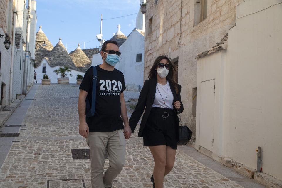 ALBEROBELLO, ITALY - MAY 24: A couple of engaged couples with a mask stroll together in the historic center of the Trulli on May 24, 2020 in Alberobello, Italy. Restaurants, bars, cafes, hairdressers and other shops have reopened, subject to social distancing measures, after more than two months of a nationwide lockdown meant to curb the spread of Covid-19. (Photo by Donato Fasano/Getty Images)