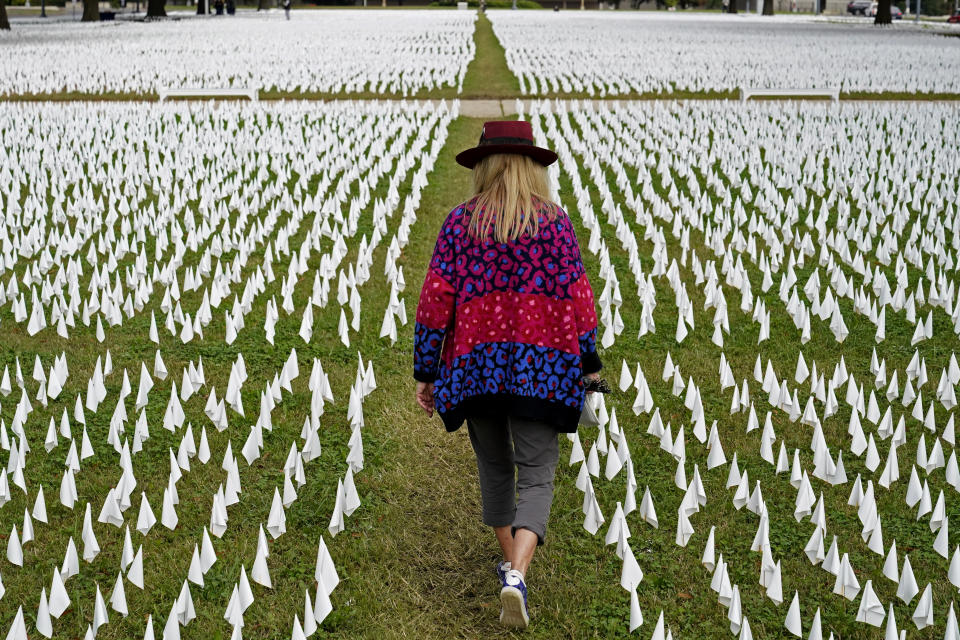 Artist Suzanne Brennan Firstenberg walks among thousands of white flags planted in remembrance of Americans who have died of COVID-19, Tuesday, Oct. 27, 2020, near Robert F. Kennedy Memorial Stadium in Washington. Firstenberg's temporary art installation, called "In America, How Could This Happen," will include an estimated 240,000 flags when completed. (AP Photo/Patrick Semansky)