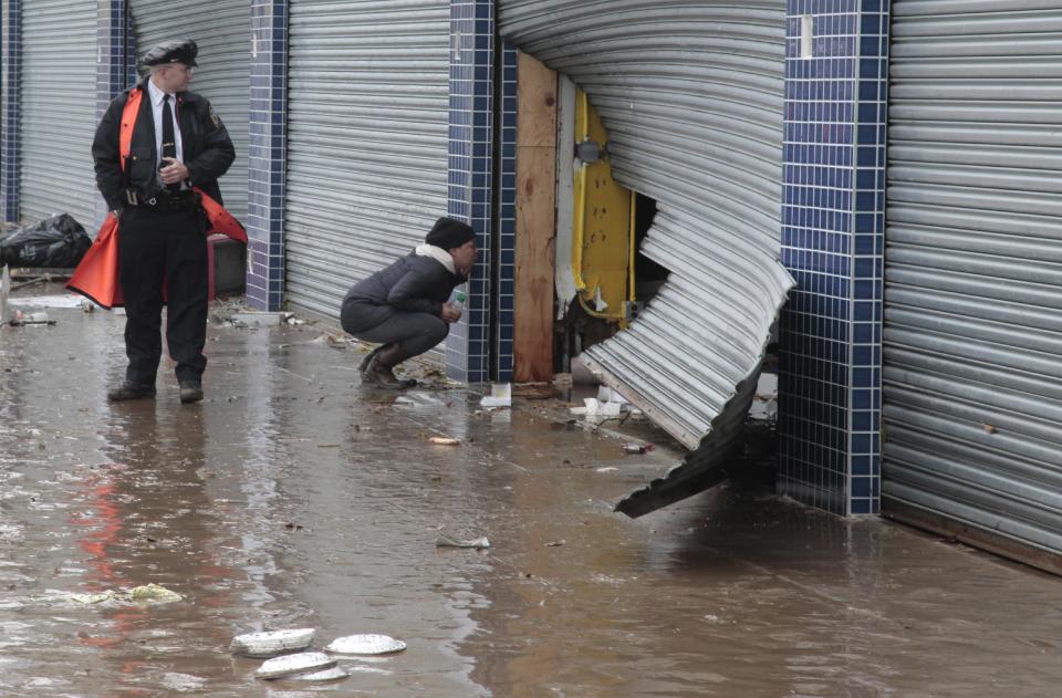 A police officer watch as a passerby look into a store through a damaged security grate, in the aftermath of Hurricane Sandy on Tuesday, Oct. 30, 2012, on Mermaid Avenue in Coney Island, N.Y. Sandy, the storm that made landfall Monday, caused multiple fatalities, halted mass transit and cut power to more than 6 million homes and businesses.(AP Photo/Bebeto Matthews)