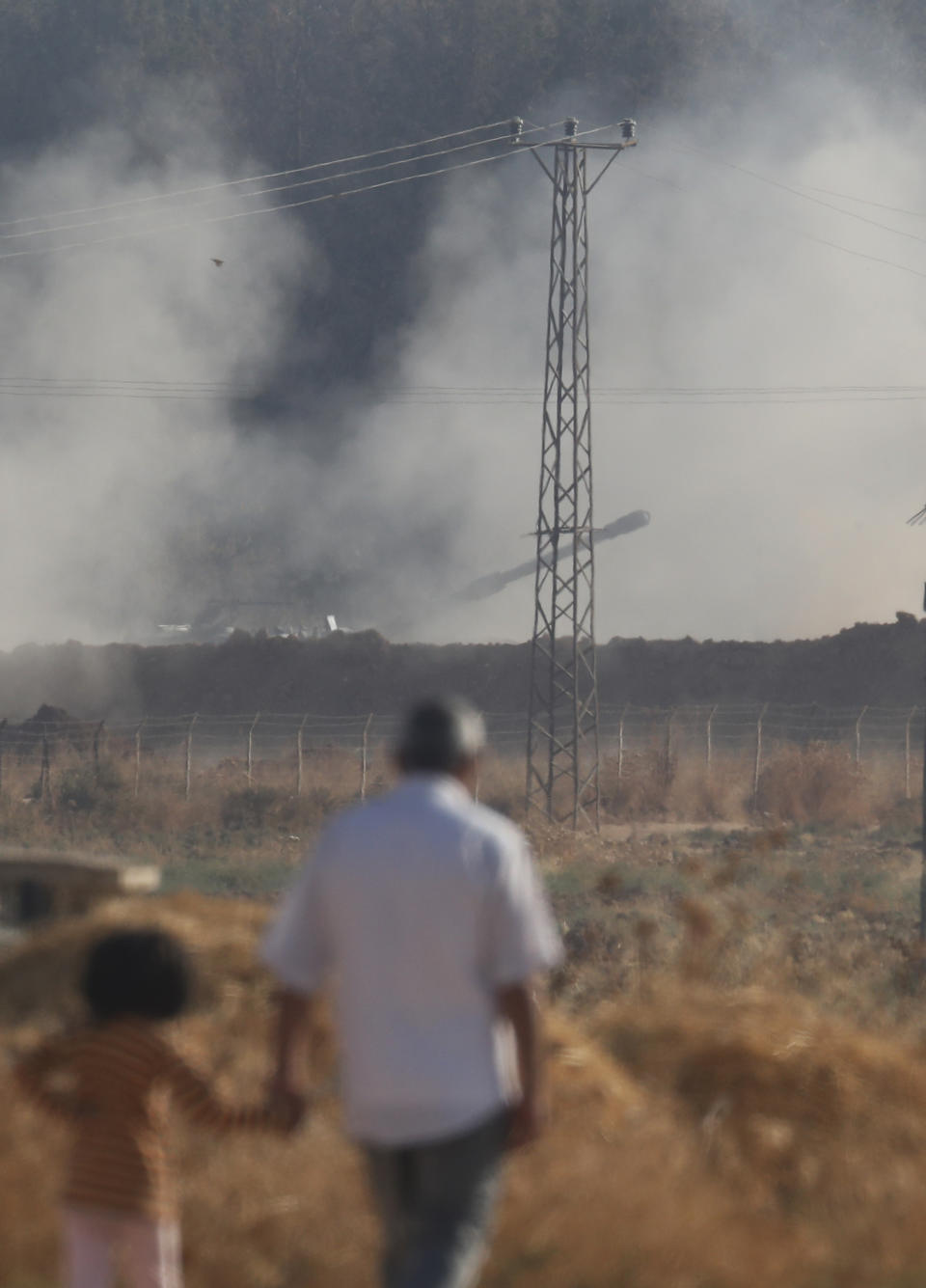 People walk in Akcakale, Sanliurfa province, southeastern Turkey, as in the background, Turkish forces artillery pieces fire targets towards Syria, Friday, Oct. 11, 2019.(AP Photo/Lefteris Pitarakis)