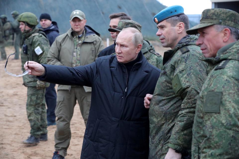 Russian President Vladimir Putin gestures in a black coat beside men in camouflage