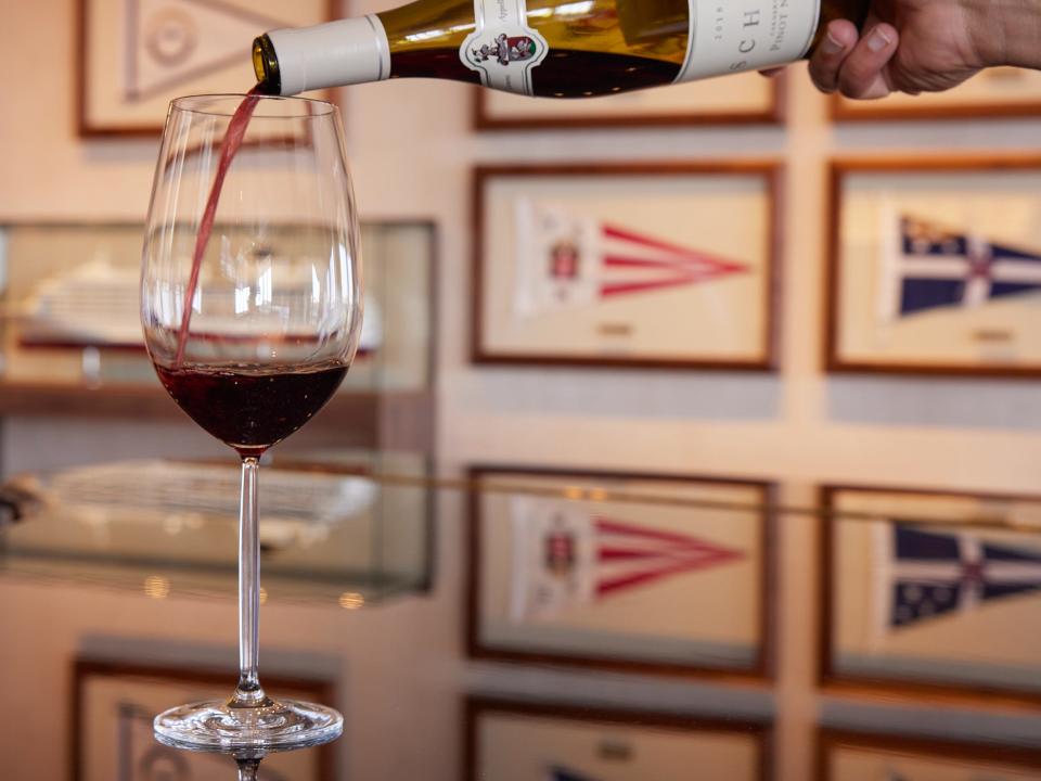 A bottle of wine being poured into a glass in a room decorated with pictures of flags.