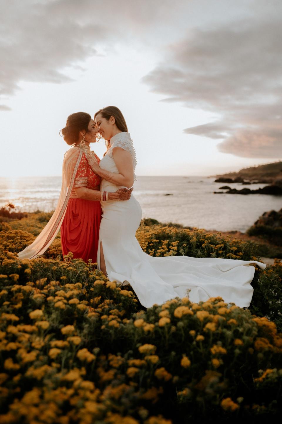 Two brides kiss in a field full of yellow flowers.