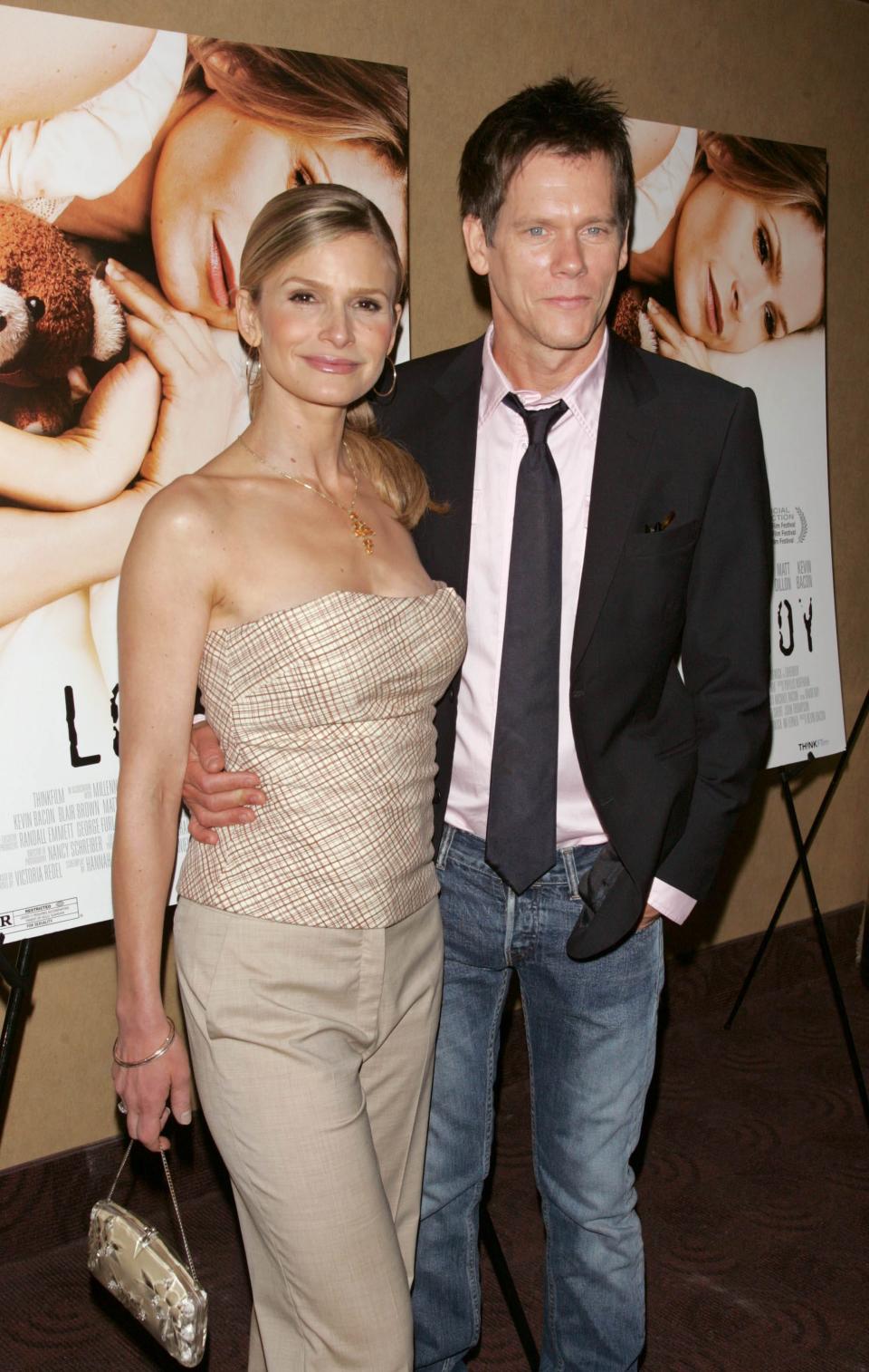 Kyra Sedgwick and Kevin Bacon standing in front of posters for the movie Loverboy