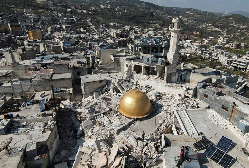 People stand near a damaged mosque in rebel-held al-Maland village