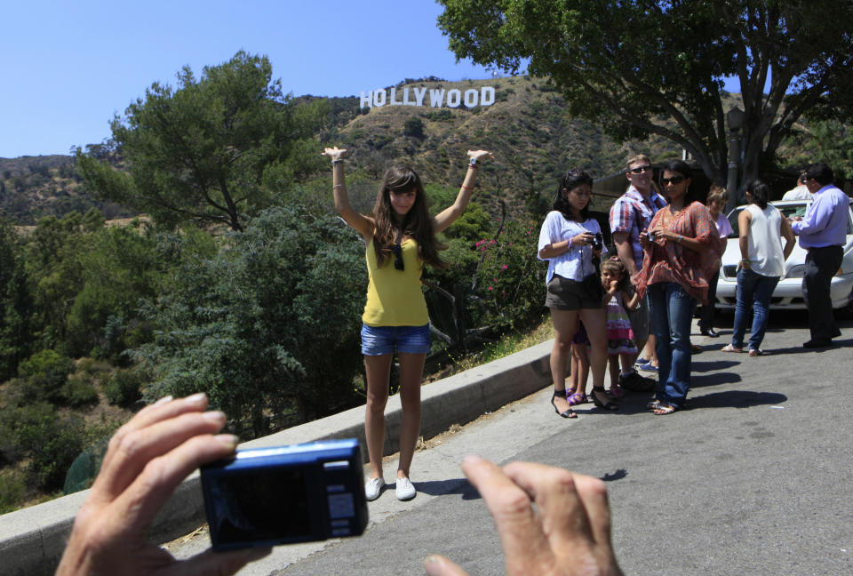 In this July 13, 2011 photo, tourists photograph each other on a hill with a view of the Hollywood sign in Los Angeles. With more than 50 miles of free hiking trails, many of them winding through chaparral-covered canyons and over hillsides, Griffith Park bills itself as the largest urban wilderness in the United States. (AP Photo/Damian Dovarganes, File)