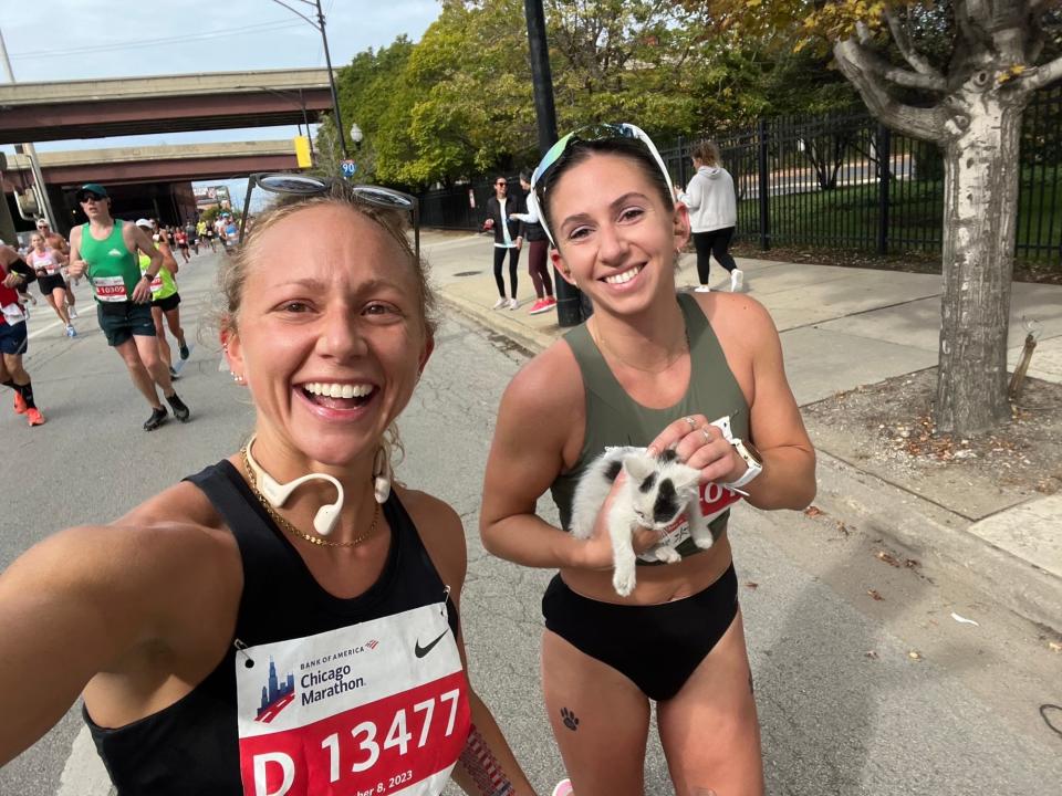 Two runners pose for a selfie, one of them holding a black-and-white kitten.