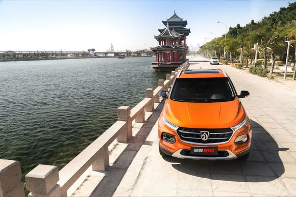 An orange Baojun 510, a small SUV, parked next to a river.