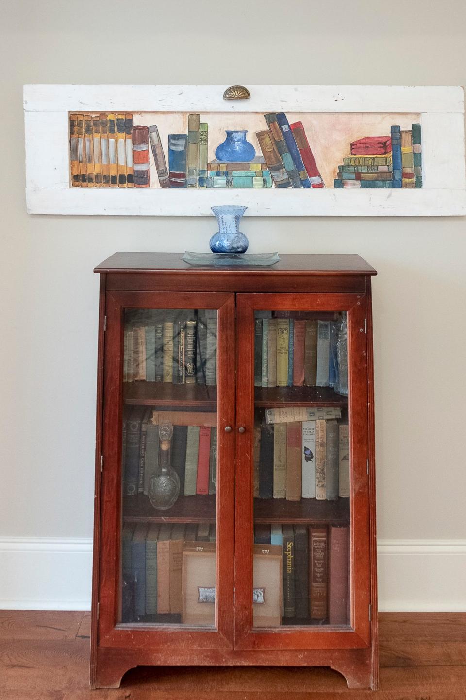 A vintage bookcase, along with some pleasing folk art, decorate the front entryway of the home.