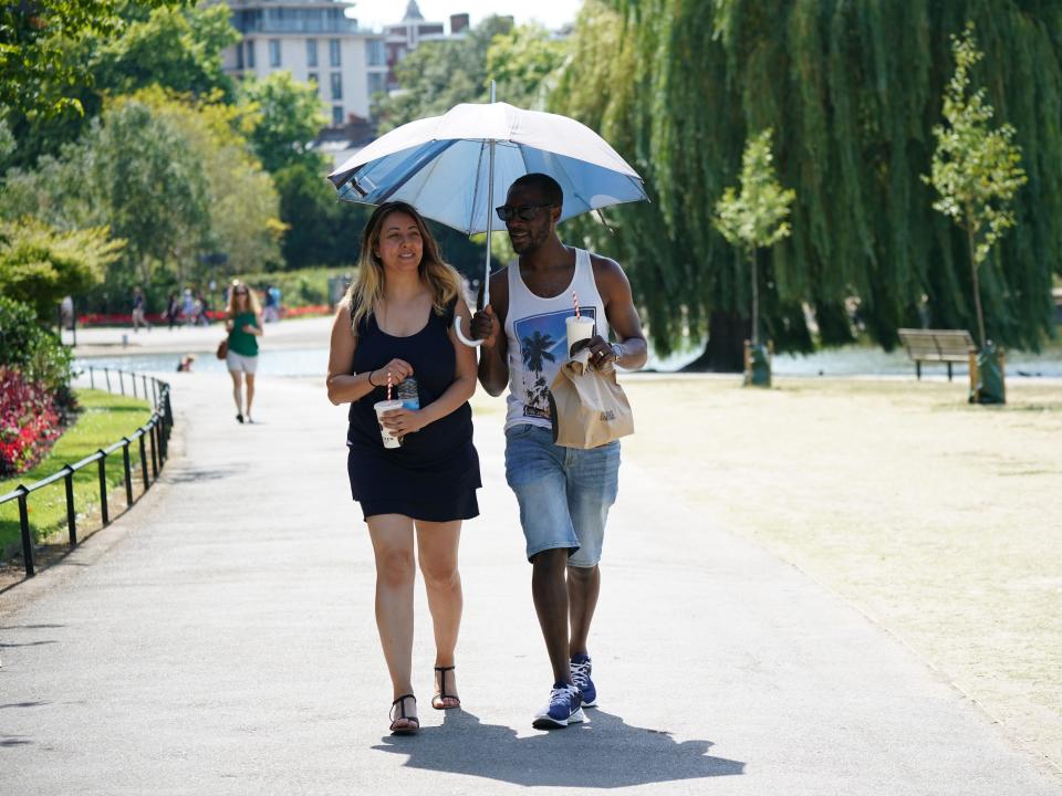 Two people stand under an umbrella in the heat.