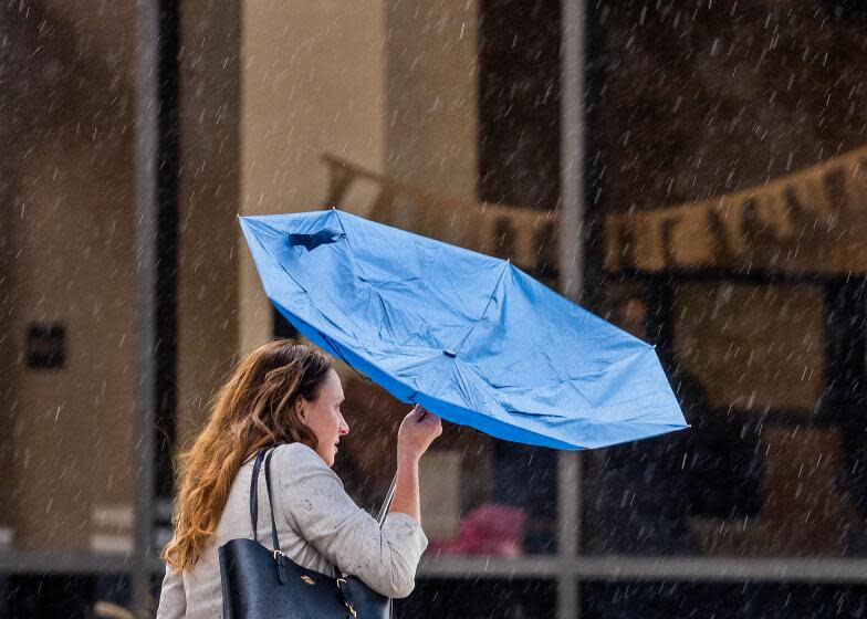 Long Beach, CA - March 06: A woman's umbrella gets flipped upside down amid a gust of wind and rain in downtown Long Beach Wednesday, March 6, 2024. (Allen J. Schaben / Los Angeles Times)