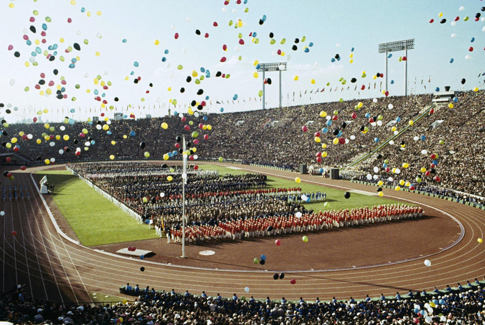 FILE - In this Oct. 10, 1964, file photo, balloons fly over Olympians and spectators during the opening ceremony of the 1964 Summer Olympics at the National Stadium in Tokyo. The famous 1964 Tokyo Olympics highlighted Japan’s resiliency. It was a prospering country that was showing off bullet trains, transistor radios, and a restored reputation just 19 years after devastating defeat in World War II. Now Japan and Tokyo are on display again, attempting to stage the postponed 2020 Tokyo Olympics in the midst of a once-in-a century pandemic. (AP Photo, File)