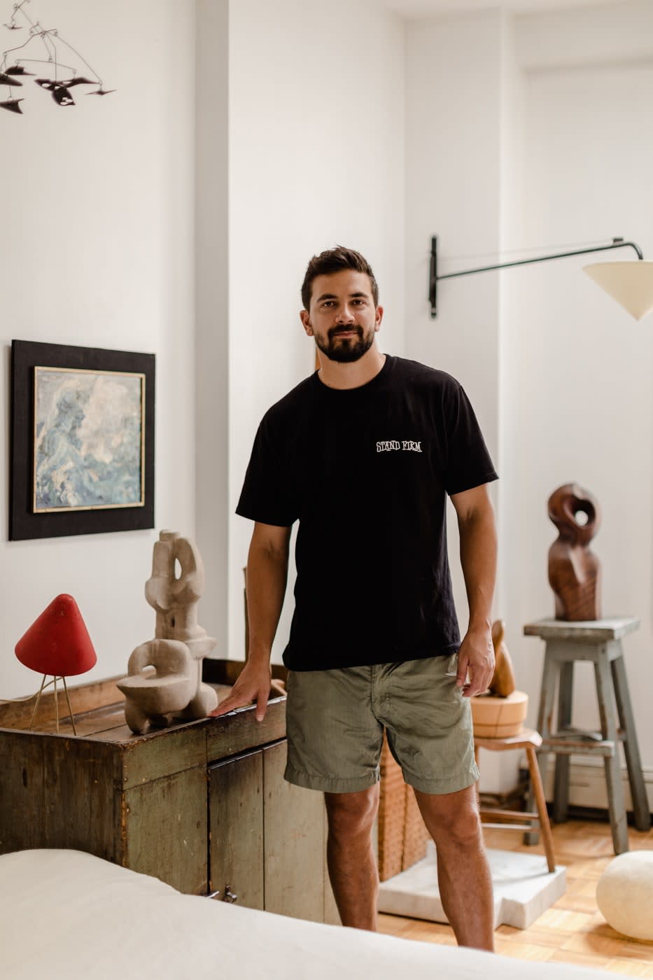 “I kind of like being a jack-of-all-trades, being able to move throughout the design world organically,” says Jonny Ribeiro, a designer, collector, and dealer. He’s pictured here in his Brooklyn apartment, with a 1960s metal lamp, a 1970s stone sculpture by Bernice Dritz-Epstein, and an impressionist seascape by Uta Von Bern.