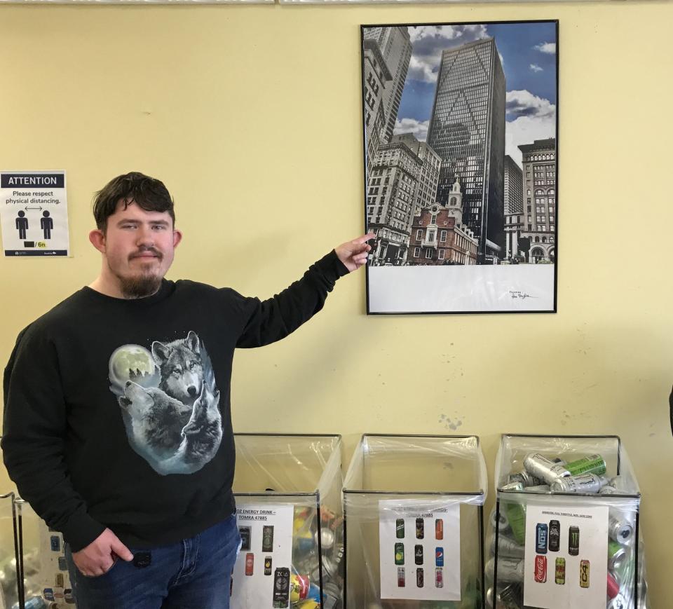 Town Line Redemption Center employee Zachary Taylor on Wednesday Feb. 8, 2023, points to a photograph he took of the Old Historic State House in Boston that is hanging on the wall of the redemption center in Dighton.
