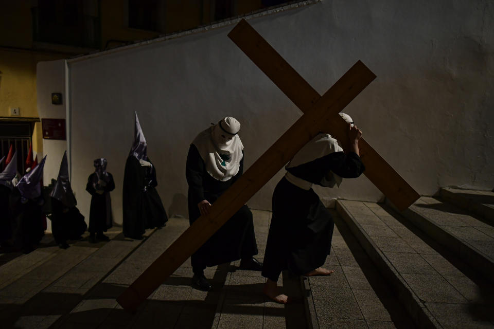 Hooded penitent from the "Santa Veracruz" brotherhood carries a cross while taking part in a Holy Week procession as people look on, in Calahorra, northern Spain, Wednesday, April 5, 2023. (AP Photo/Alvaro Barrientos)