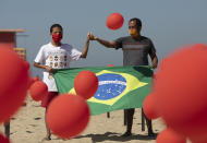 Marcio Antonio do Nascimento, right, and Lucas Cruz, the father and brother of 25-year-old Hugo do Nascimento who died from the new coronavirus, hold a Brazilian national flag as red balloons are released to honor the victims of COVID-19 in a demonstration organized by Rio de Paz, on Copacabana beach in Rio de Janeiro, Brazil, Saturday, Aug. 8, 2020, as the country heads to a milestone of 100,000 coronavirus related deaths. (AP Photo/Silvia Izquierdo)