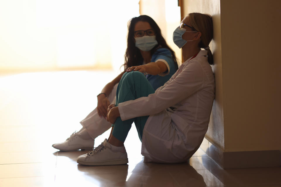 Tired women doctors are sitting in masks in corridor. Burnout of healthcare workers concept