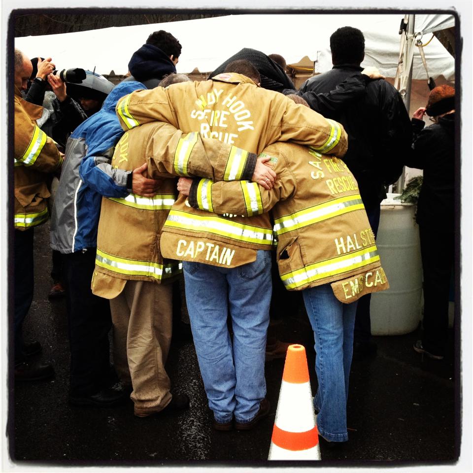 Firefighters with their arms around each other observe a moment of silence near the entrance to Sandy Hook Elementary School.