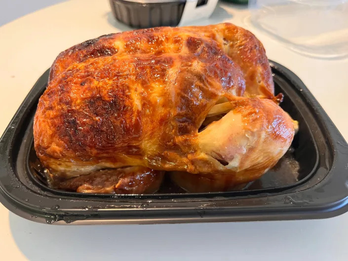 Large whole rotisserie chicken in a black container on a white table