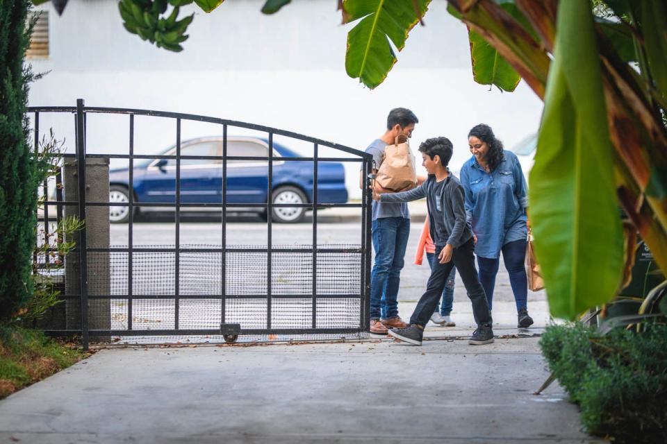 A family pushes a black gate open to bring in a shopping bag.