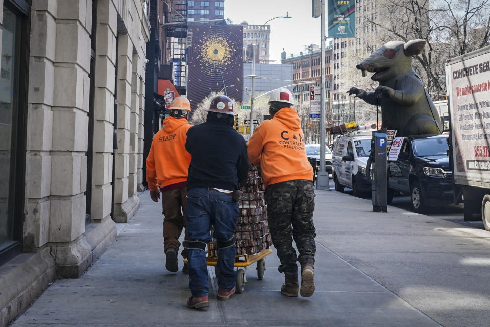 Construction workers push a cart of bricks towards Scabby, right, a giant inflatable rat used by organized labor, standing in protest outside a Petco on Wednesday March 29, 2023, in New York. For decades, inflatable rats like Scabby have been looming over union protests, drawing attention to construction sites or companies with labor disputes. (AP Photo/Bebeto Matthews)