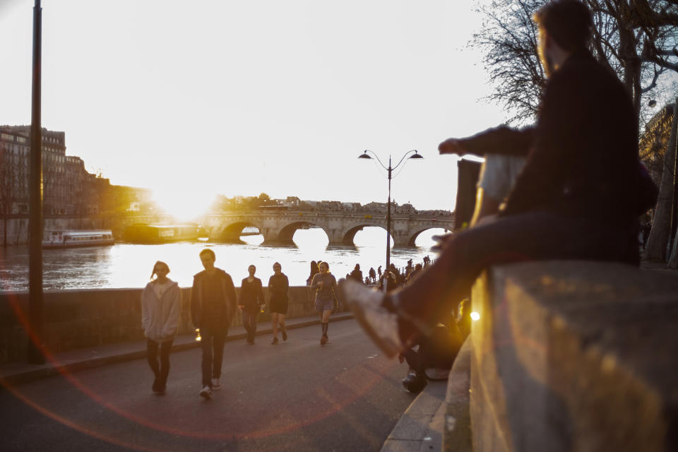 People stroll along the Seine river banks at sunset Sunday March 15, 2020 in Paris. For most people, the new coronavirus causes only mild or moderate symptoms. For some it can cause more severe illness. (AP Photo/Rafael Yaghobzadeh)